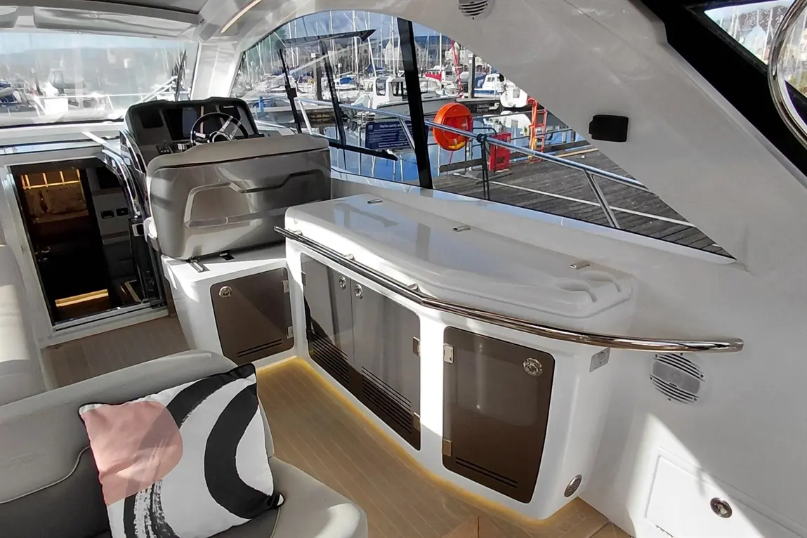 Modern yacht interior featuring a helm, stylish storage cabinets, and a cushion with abstract patterns, overlooking a marina.